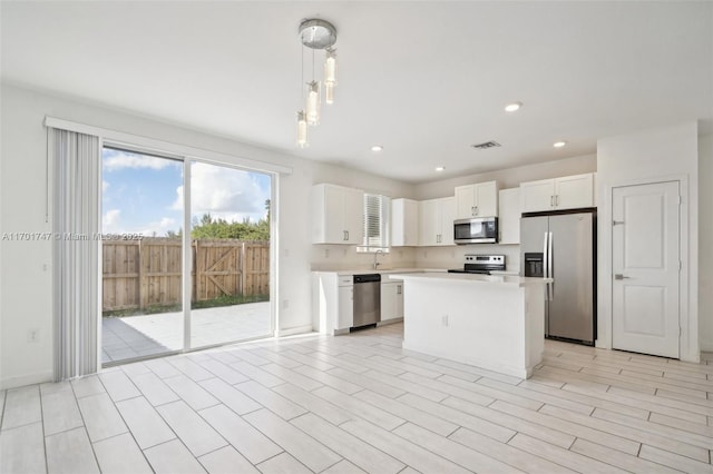 kitchen with appliances with stainless steel finishes, sink, a center island, decorative light fixtures, and white cabinets