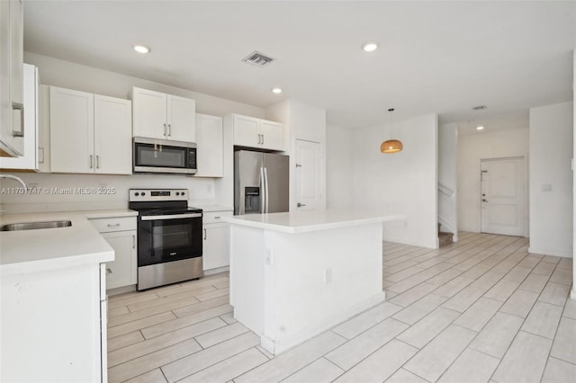 kitchen featuring hanging light fixtures, a kitchen island, sink, appliances with stainless steel finishes, and white cabinets