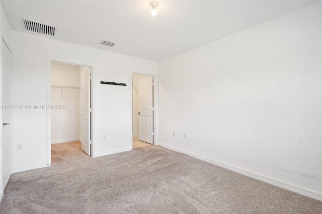 unfurnished bedroom featuring a closet, light colored carpet, and a walk in closet