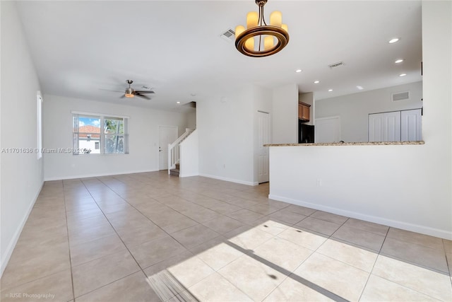 empty room with light tile patterned floors and ceiling fan with notable chandelier