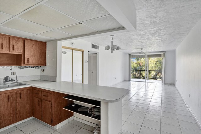 kitchen with a notable chandelier, kitchen peninsula, sink, and light tile patterned floors