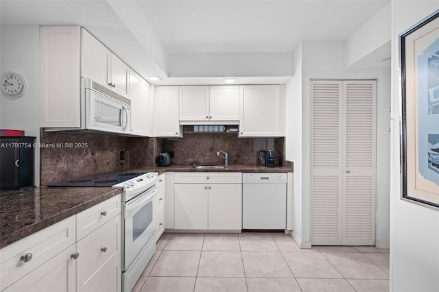 kitchen with white appliances, light tile patterned floors, dark stone counters, sink, and white cabinetry