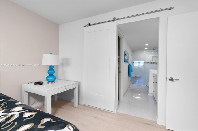 bedroom featuring ensuite bath, light wood-type flooring, and a barn door