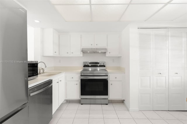 kitchen with a paneled ceiling, stainless steel appliances, sink, light tile patterned floors, and white cabinets