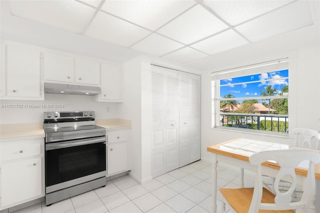 kitchen featuring light tile patterned floors, a drop ceiling, white cabinetry, and stainless steel range with electric stovetop