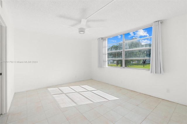 empty room featuring ceiling fan, light tile patterned flooring, and a textured ceiling