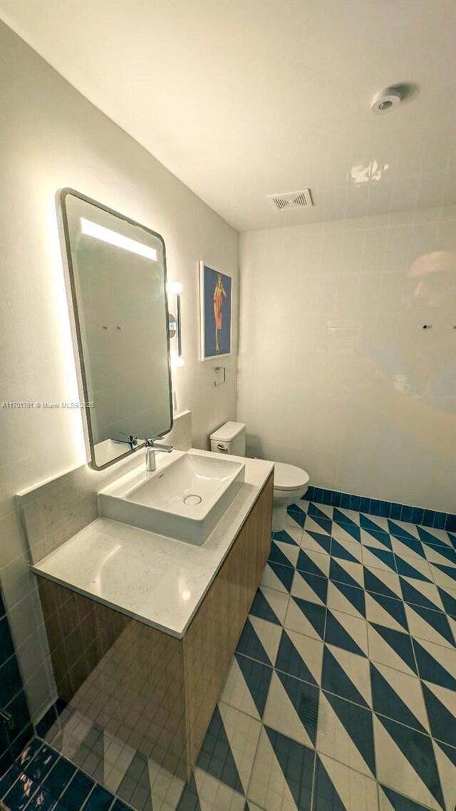 bathroom featuring tile patterned flooring, sink, tile walls, and toilet