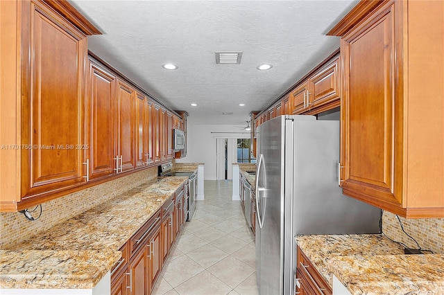 kitchen with appliances with stainless steel finishes, a textured ceiling, tasteful backsplash, and light stone counters