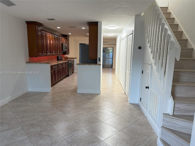 kitchen with appliances with stainless steel finishes, light tile patterned floors, and dark stone counters