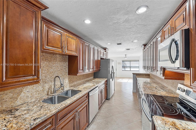 kitchen with light tile patterned flooring, stainless steel appliances, light stone counters, and sink