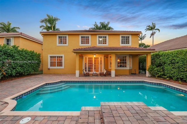 pool at dusk with french doors and a patio