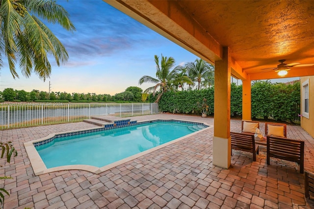 pool at dusk featuring ceiling fan, a water view, and a patio