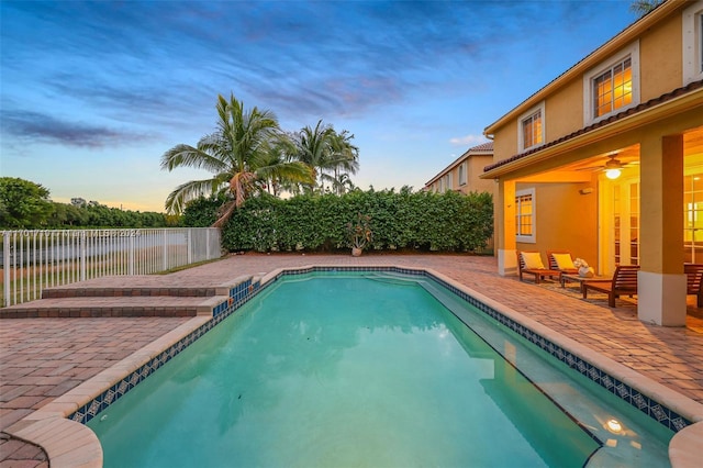 pool at dusk featuring ceiling fan and a patio area