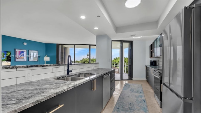 kitchen featuring sink, backsplash, expansive windows, stainless steel appliances, and light stone countertops