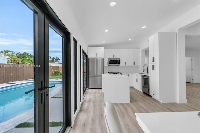 kitchen with sink, light hardwood / wood-style flooring, appliances with stainless steel finishes, a kitchen island, and white cabinetry