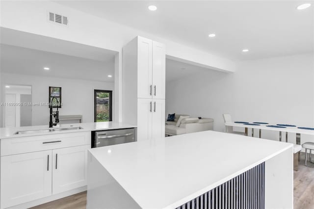 kitchen with sink, dishwasher, white cabinets, and light hardwood / wood-style flooring