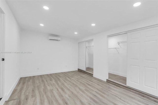 unfurnished bedroom featuring light hardwood / wood-style floors, a wall unit AC, and multiple closets