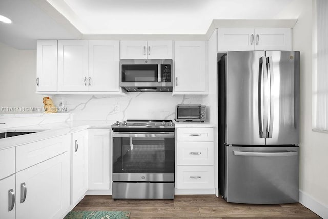 kitchen featuring tasteful backsplash, light stone counters, stainless steel appliances, dark wood-type flooring, and white cabinetry