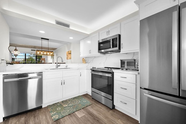 kitchen with sink, dark hardwood / wood-style floors, kitchen peninsula, white cabinets, and appliances with stainless steel finishes