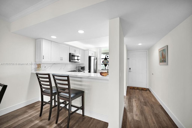 kitchen with a breakfast bar, white cabinets, dark hardwood / wood-style floors, appliances with stainless steel finishes, and kitchen peninsula