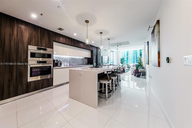 kitchen featuring white cabinetry, hanging light fixtures, a kitchen bar, a kitchen island with sink, and light tile patterned flooring