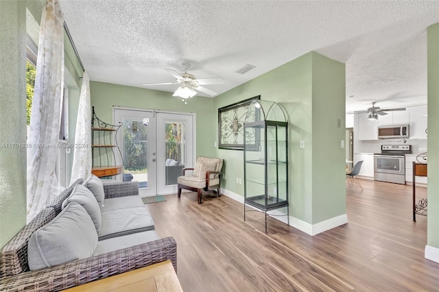 living room with french doors, light wood-type flooring, a textured ceiling, and ceiling fan