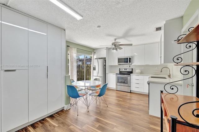 kitchen with appliances with stainless steel finishes, ceiling fan, sink, light hardwood / wood-style flooring, and white cabinets