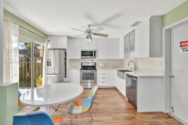 kitchen with white cabinets, ceiling fan, light wood-type flooring, a textured ceiling, and stainless steel appliances