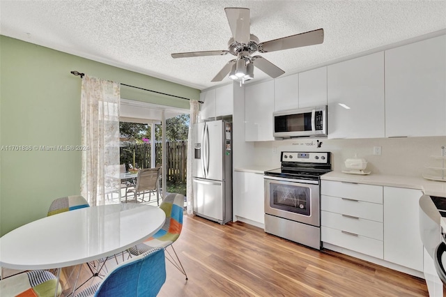 kitchen featuring light wood-type flooring, a textured ceiling, stainless steel appliances, ceiling fan, and white cabinets