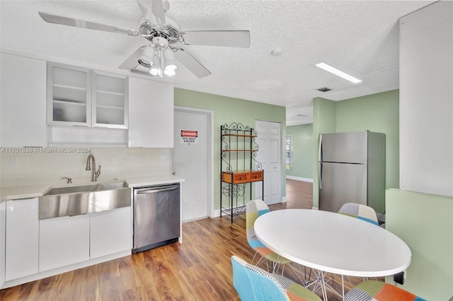 kitchen featuring sink, stainless steel appliances, light hardwood / wood-style floors, a textured ceiling, and white cabinets