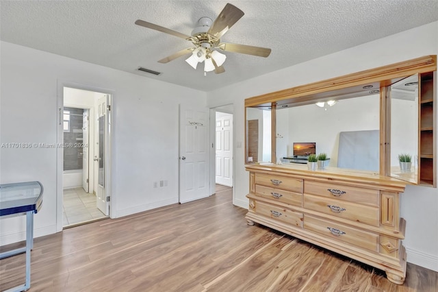 bedroom with ensuite bathroom, ceiling fan, light wood-type flooring, and a textured ceiling