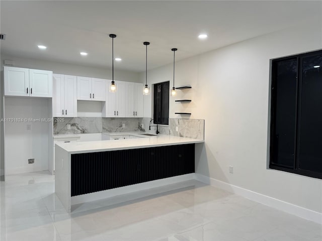 kitchen featuring tasteful backsplash, baseboards, a peninsula, white cabinetry, and a sink