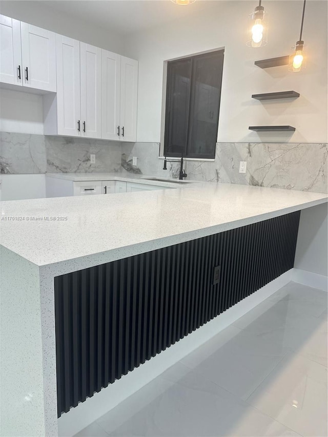 kitchen with light stone counters, backsplash, white cabinets, a sink, and a peninsula