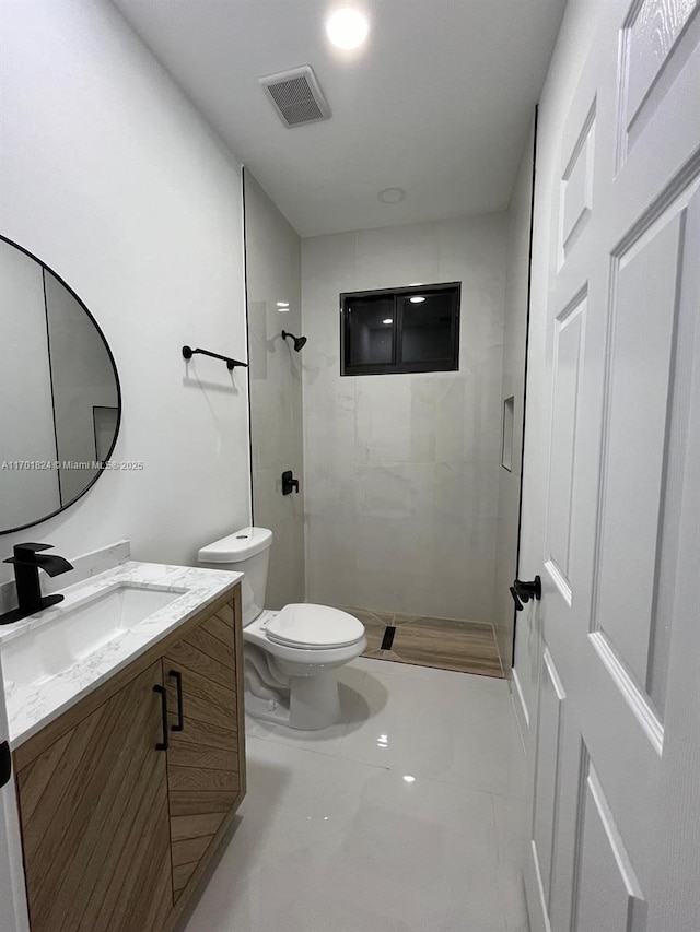 full bathroom featuring visible vents, a tile shower, vanity, and toilet