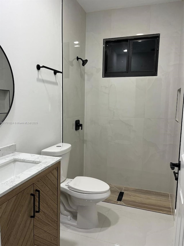 full bath featuring a tile shower, vanity, and toilet