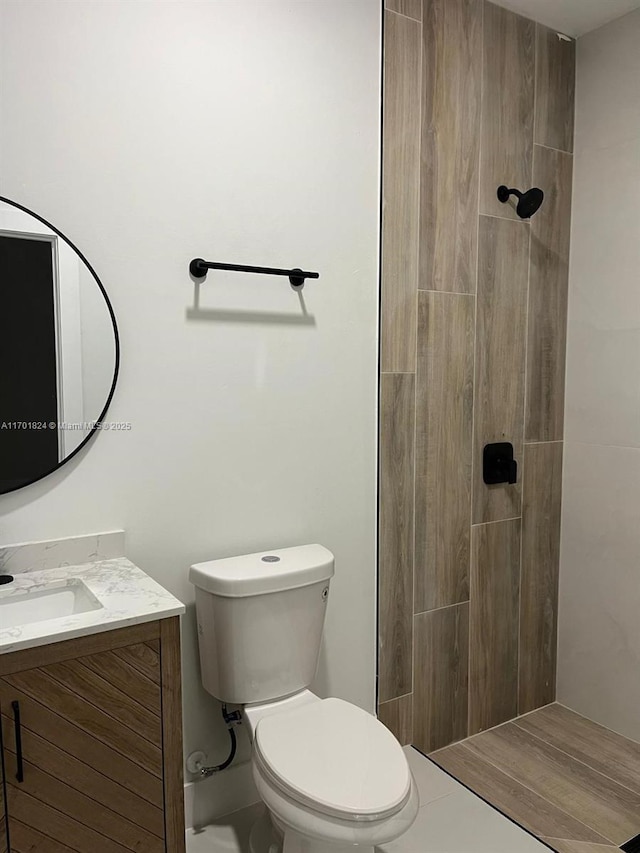 bathroom featuring a tile shower, vanity, and toilet