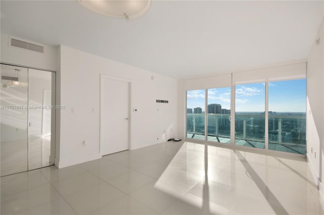 empty room featuring a wall of windows and light tile patterned floors