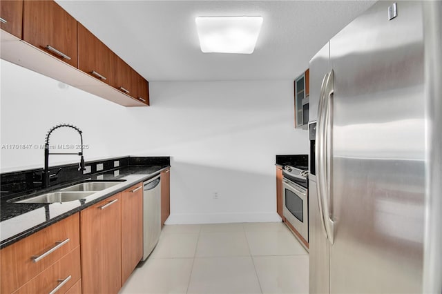 kitchen with light tile patterned flooring, appliances with stainless steel finishes, sink, and dark stone counters