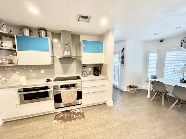 kitchen with white cabinets, wall chimney exhaust hood, stainless steel oven, and black electric cooktop