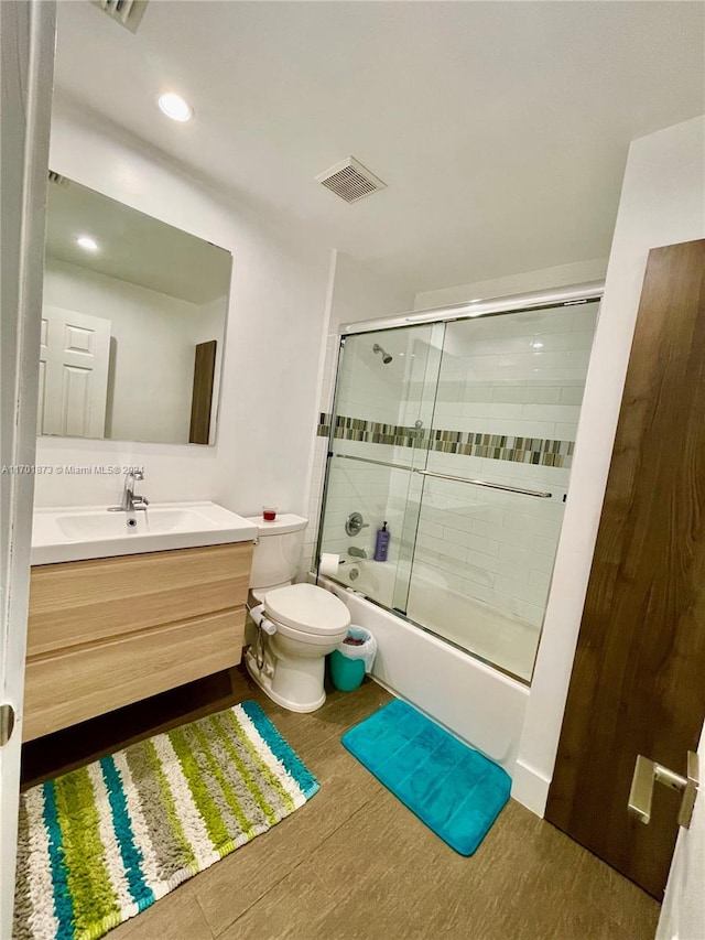 full bathroom featuring hardwood / wood-style floors, vanity, toilet, and bath / shower combo with glass door