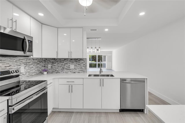 kitchen with white cabinets, a raised ceiling, sink, appliances with stainless steel finishes, and light hardwood / wood-style floors