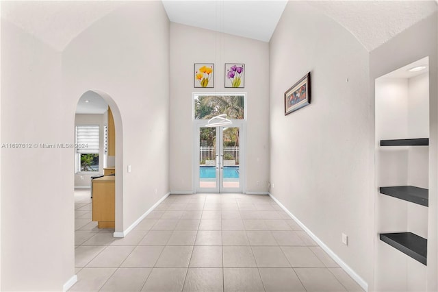 hall with light tile patterned flooring, high vaulted ceiling, and french doors