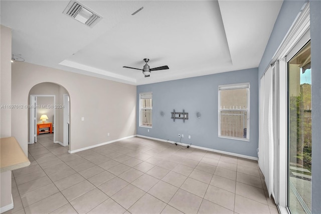 tiled empty room featuring ceiling fan and a raised ceiling