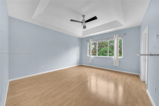 empty room with ceiling fan, light hardwood / wood-style floors, and a tray ceiling