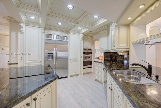 kitchen featuring sink, built in fridge, dark stone countertops, decorative backsplash, and light wood-type flooring