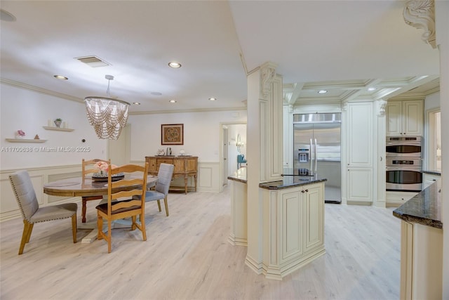 kitchen with pendant lighting, ornamental molding, stainless steel appliances, light wood-type flooring, and cream cabinetry