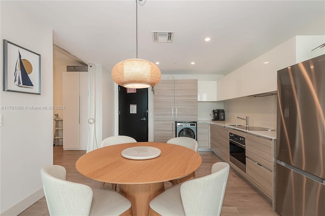 kitchen featuring stainless steel appliances, light hardwood / wood-style flooring, pendant lighting, washer / dryer, and white cabinets