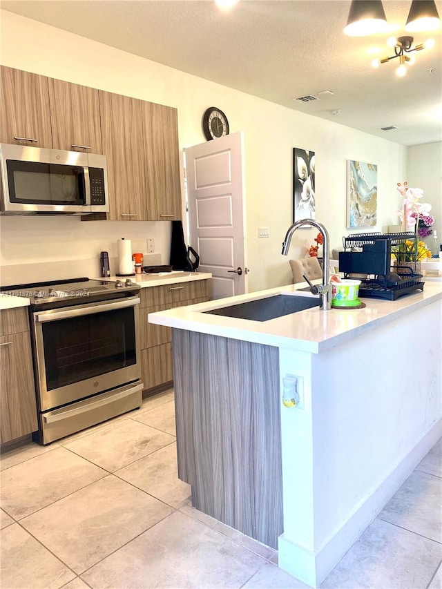 kitchen featuring appliances with stainless steel finishes, a textured ceiling, a kitchen island with sink, sink, and light tile patterned floors