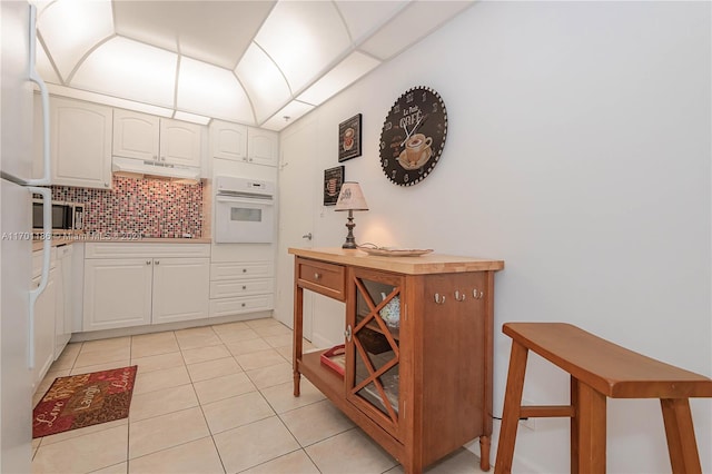 kitchen featuring decorative backsplash, light tile patterned floors, white oven, and white cabinetry