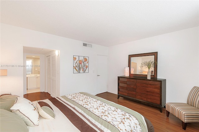 bedroom with ensuite bathroom and dark wood-type flooring